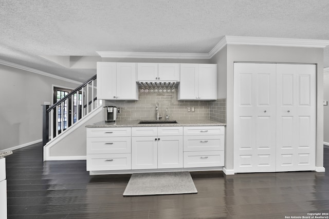 kitchen with white cabinetry, dark hardwood / wood-style flooring, sink, light stone countertops, and backsplash