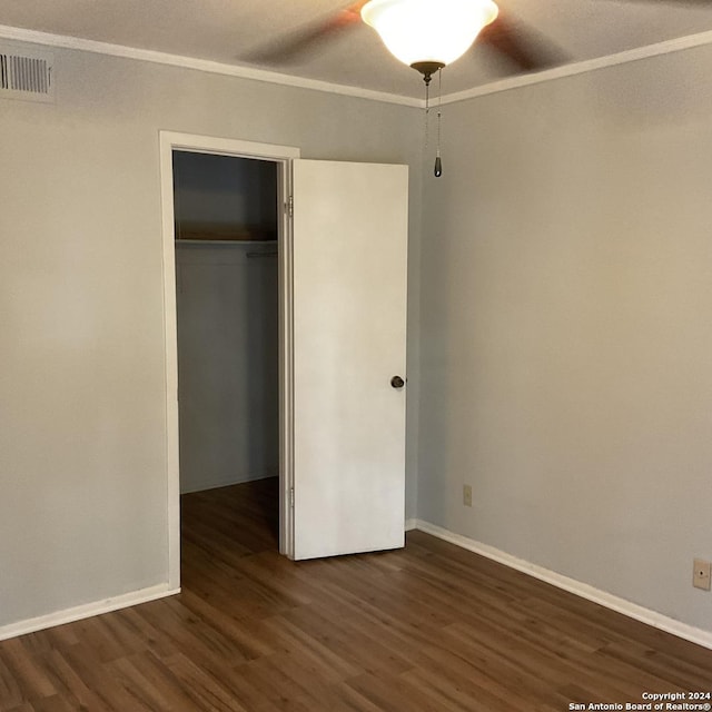 unfurnished bedroom featuring a walk in closet, crown molding, ceiling fan, dark hardwood / wood-style flooring, and a closet