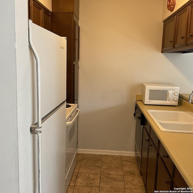 kitchen featuring dark brown cabinets, sink, white appliances, and tile patterned flooring