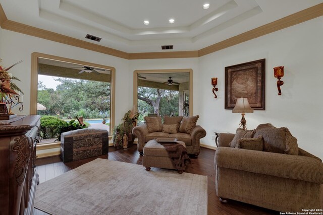 living room featuring ceiling fan, dark wood-type flooring, a brick fireplace, and a tray ceiling