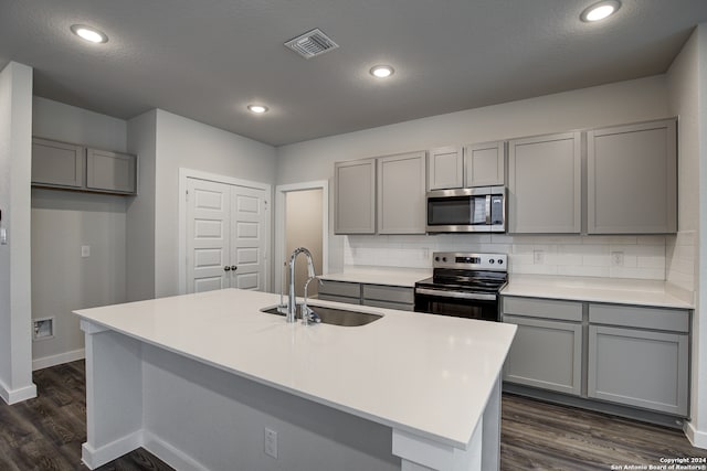 kitchen with gray cabinetry, sink, stainless steel appliances, tasteful backsplash, and an island with sink