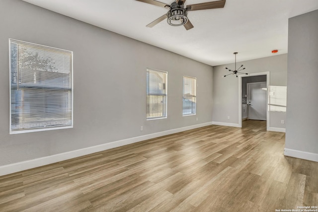 unfurnished room with ceiling fan with notable chandelier and light hardwood / wood-style floors