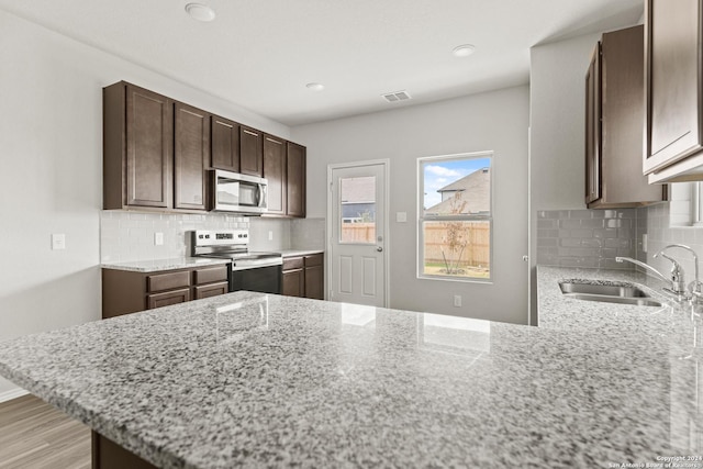 kitchen featuring appliances with stainless steel finishes, sink, kitchen peninsula, light stone countertops, and dark brown cabinets