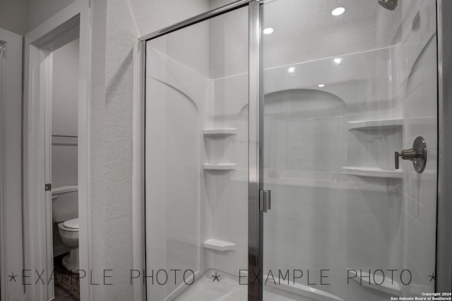 bathroom with a textured ceiling, a shower with door, and toilet