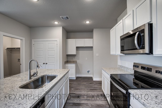 kitchen with appliances with stainless steel finishes, white cabinetry, light stone countertops, dark hardwood / wood-style flooring, and sink