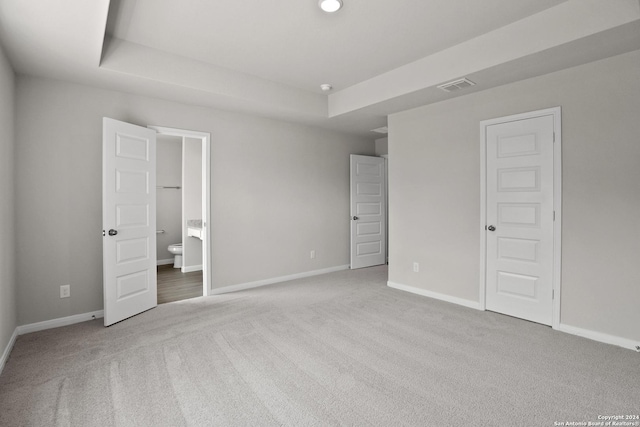 unfurnished bedroom with ensuite bath, a raised ceiling, and light carpet