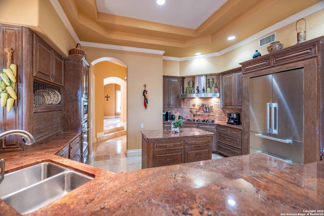 kitchen featuring built in fridge, tasteful backsplash, sink, a raised ceiling, and light stone countertops