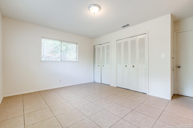 unfurnished bedroom with light tile patterned flooring and two closets