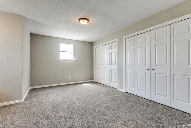 unfurnished bedroom featuring a textured ceiling, two closets, and carpet