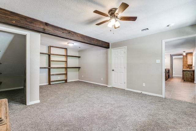 unfurnished bedroom with ensuite bath, light colored carpet, beamed ceiling, ceiling fan, and a textured ceiling