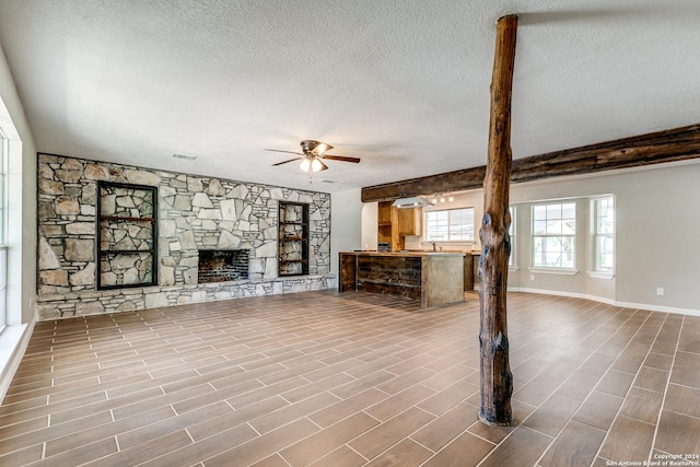 unfurnished living room featuring a textured ceiling, a fireplace, ceiling fan, beamed ceiling, and sink