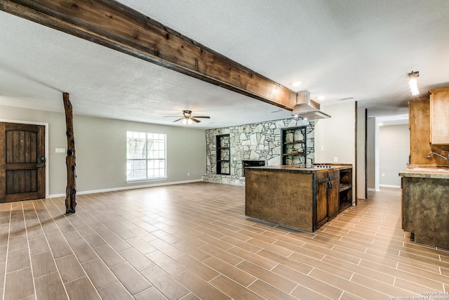 kitchen featuring ceiling fan, a stone fireplace, sink, and a textured ceiling