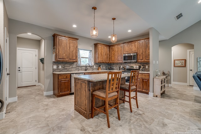 kitchen featuring stainless steel appliances, backsplash, light tile patterned floors, decorative light fixtures, and a center island