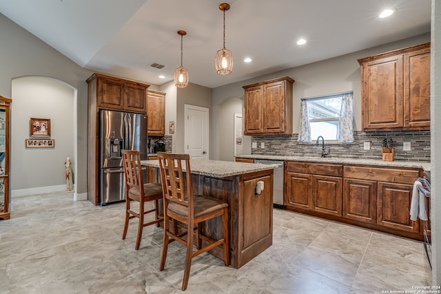 kitchen with appliances with stainless steel finishes, tasteful backsplash, sink, decorative light fixtures, and a kitchen island