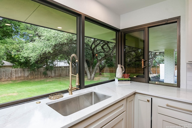 kitchen with white cabinetry, light stone counters, and sink