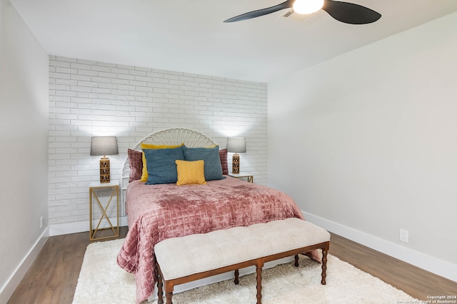 bedroom featuring hardwood / wood-style flooring, brick wall, and ceiling fan