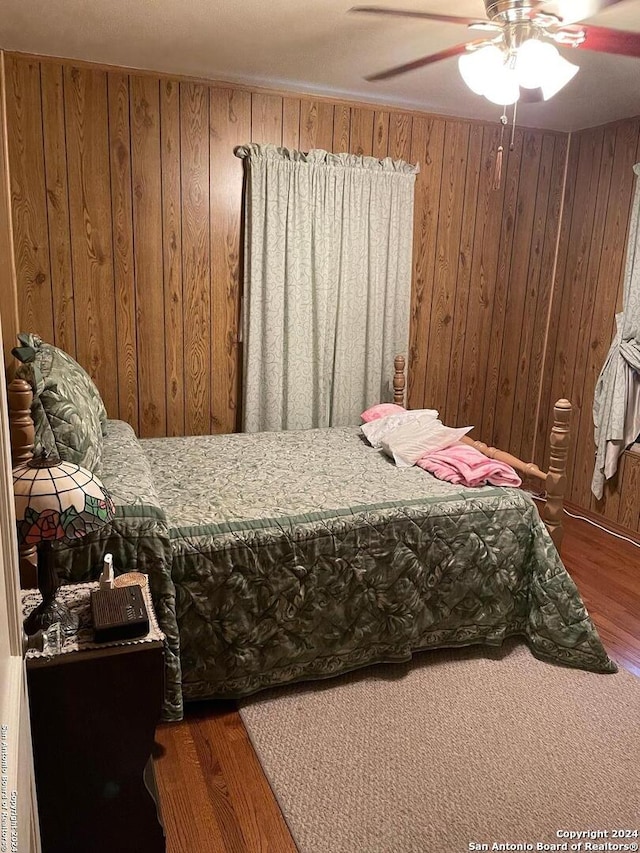 bedroom featuring ceiling fan, dark wood-type flooring, and wood walls