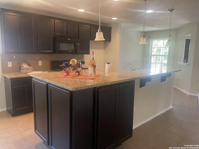 kitchen with backsplash, a center island with sink, light tile patterned floors, and decorative light fixtures