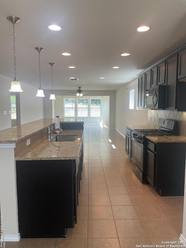 kitchen featuring sink, decorative light fixtures, decorative backsplash, a center island with sink, and black appliances