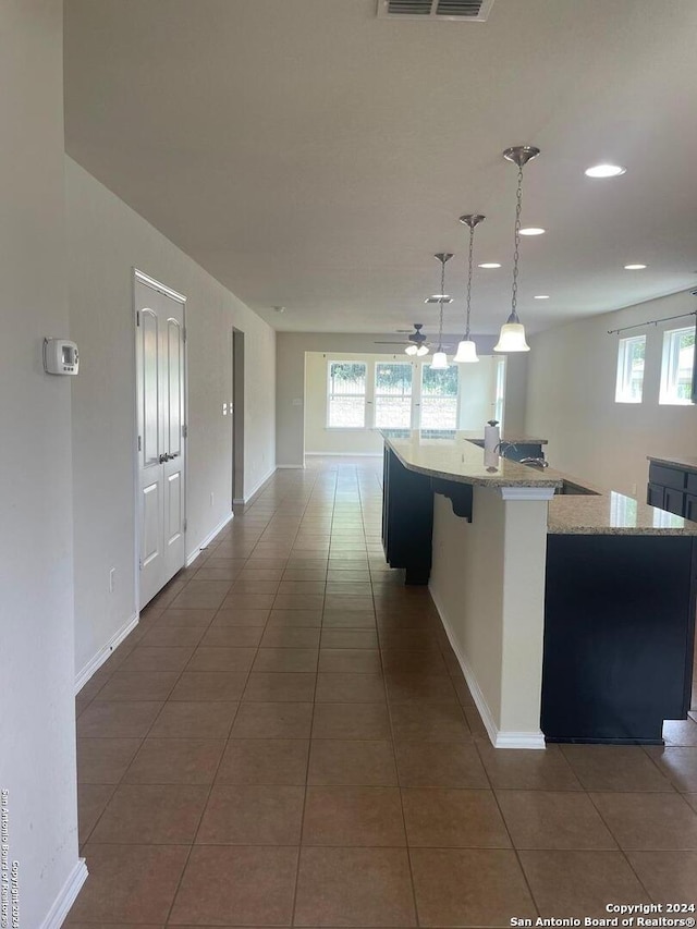 kitchen with pendant lighting, dark tile patterned flooring, ceiling fan, and a large island