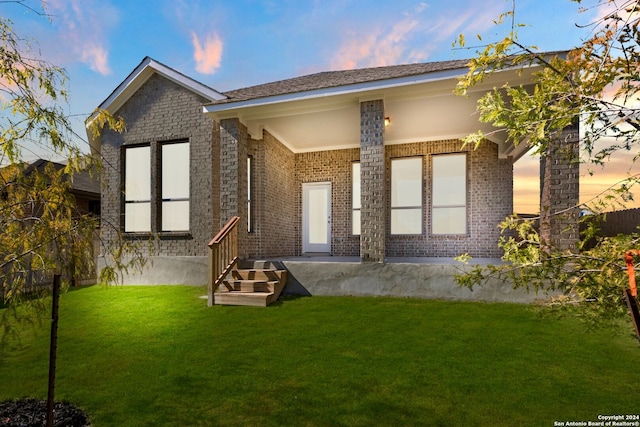 back house at dusk featuring a lawn