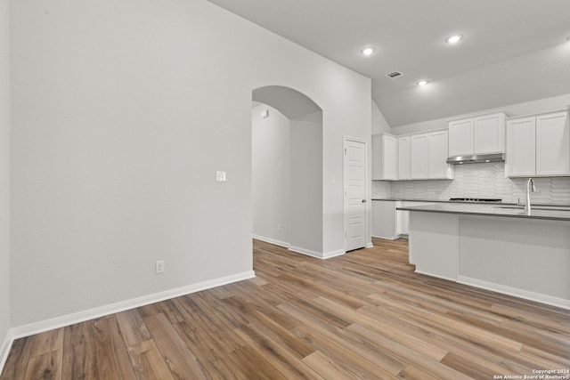 kitchen with lofted ceiling, sink, white cabinetry, tasteful backsplash, and light hardwood / wood-style floors