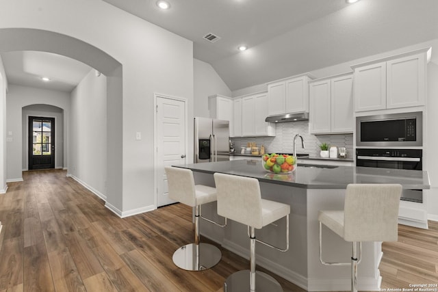 kitchen featuring built in microwave, a breakfast bar area, a center island with sink, and white cabinets