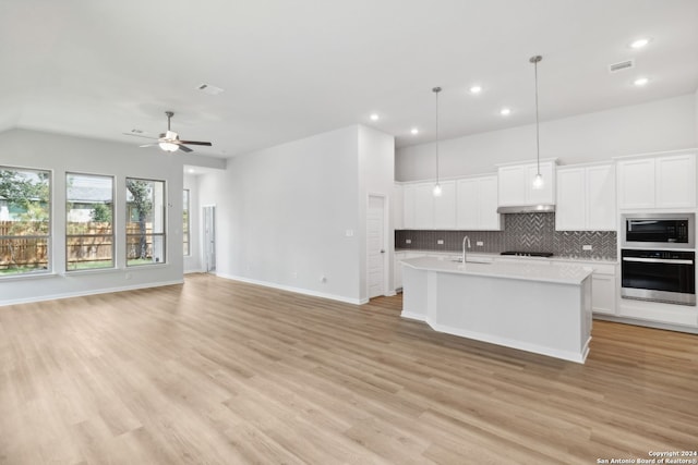 kitchen with sink, white cabinetry, an island with sink, built in microwave, and stainless steel oven