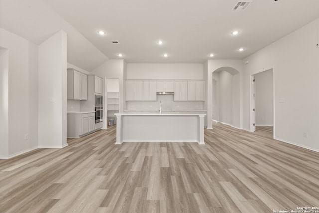 kitchen featuring light wood-type flooring, appliances with stainless steel finishes, sink, lofted ceiling, and a kitchen island with sink