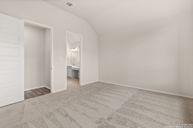 unfurnished bedroom with ensuite bathroom, carpet flooring, and vaulted ceiling