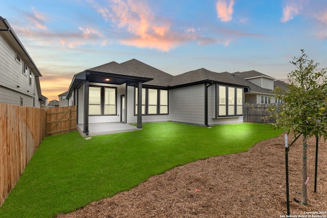 back house at dusk featuring a lawn