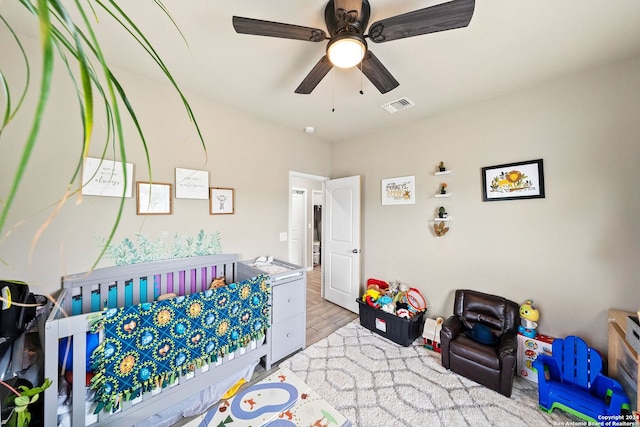 bedroom featuring a crib, light hardwood / wood-style flooring, and ceiling fan