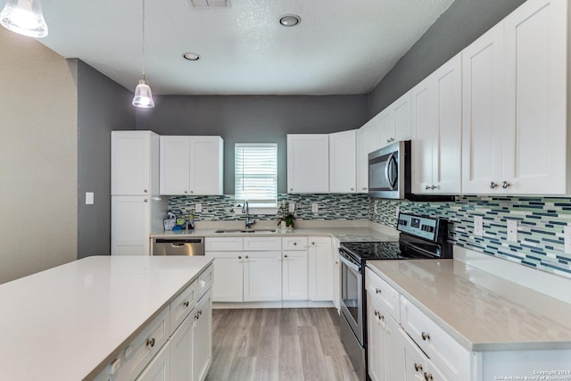 kitchen with appliances with stainless steel finishes, white cabinets, pendant lighting, light hardwood / wood-style flooring, and sink