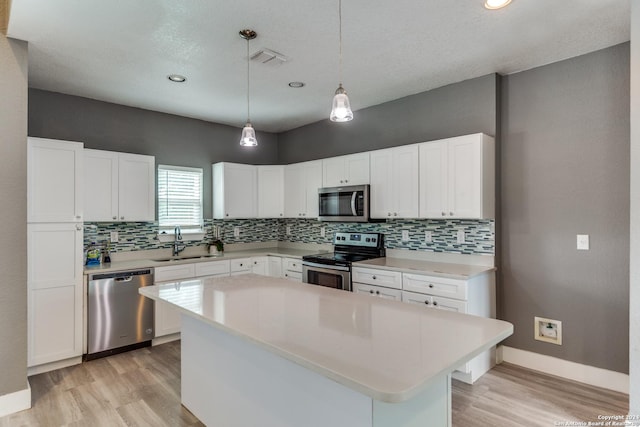 kitchen with appliances with stainless steel finishes, a kitchen island, decorative light fixtures, white cabinetry, and sink