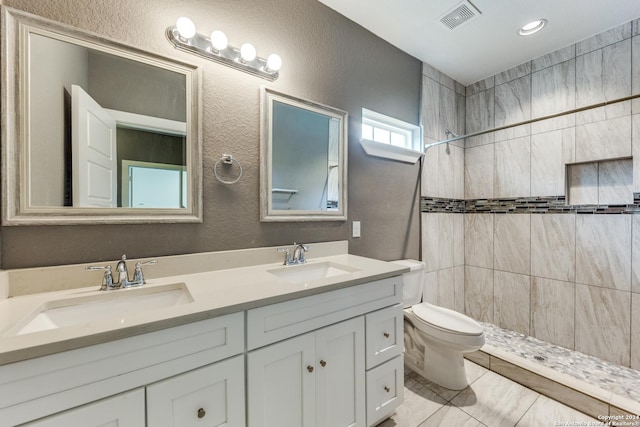 bathroom featuring toilet, vanity, tile patterned flooring, and a tile shower