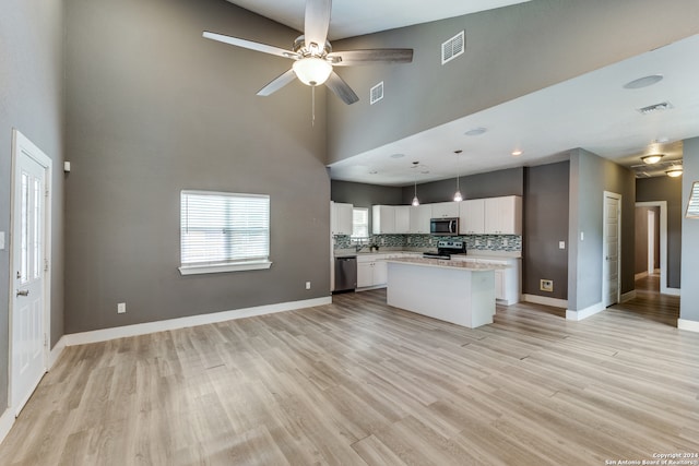 kitchen featuring hanging light fixtures, white cabinetry, appliances with stainless steel finishes, a center island, and light hardwood / wood-style floors