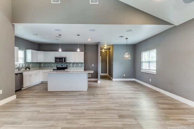 kitchen with appliances with stainless steel finishes, white cabinetry, backsplash, a center island, and decorative light fixtures