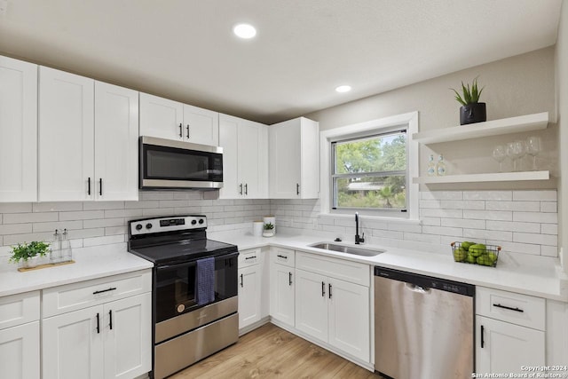 kitchen with sink, stainless steel appliances, decorative backsplash, white cabinets, and light wood-type flooring