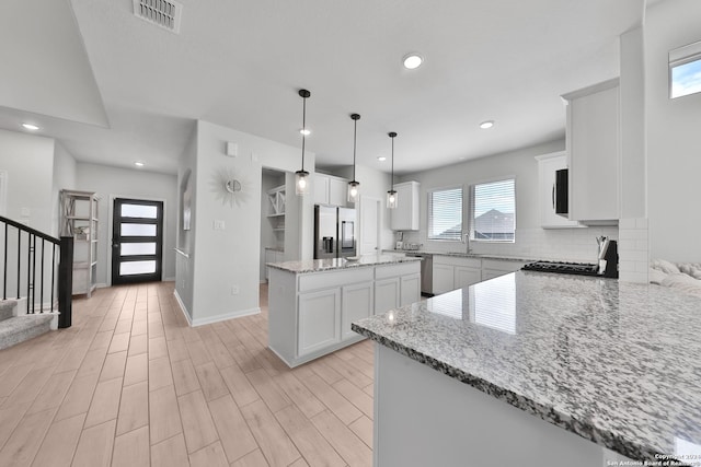 kitchen with kitchen peninsula, appliances with stainless steel finishes, light stone countertops, white cabinetry, and hanging light fixtures