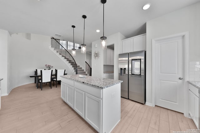 kitchen with white cabinets, stainless steel refrigerator with ice dispenser, light stone countertops, tasteful backsplash, and a kitchen island