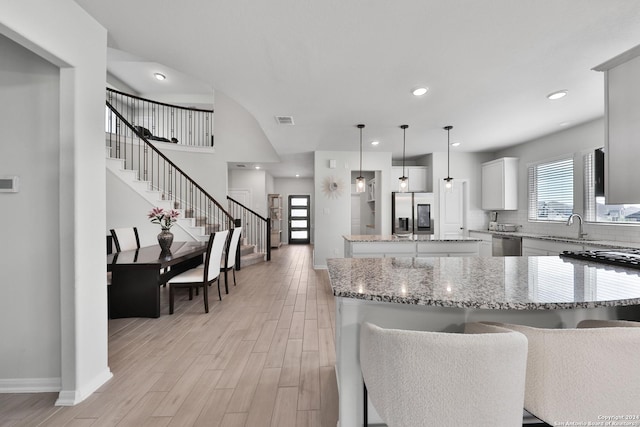 kitchen featuring light stone countertops, stainless steel appliances, decorative light fixtures, white cabinets, and a center island