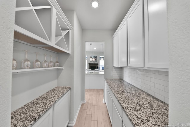 bar with backsplash, stone counters, white cabinetry, and light hardwood / wood-style flooring