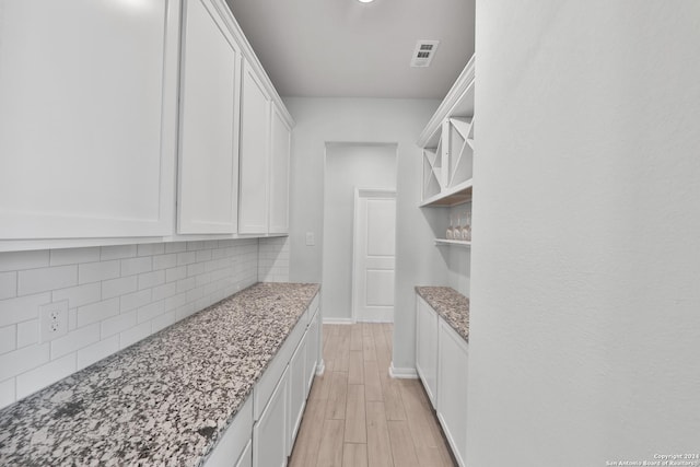 interior space with light stone countertops, decorative backsplash, light hardwood / wood-style floors, and white cabinetry