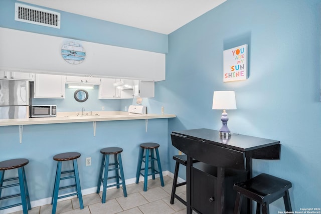 kitchen with a kitchen bar, white cabinets, kitchen peninsula, and stainless steel refrigerator