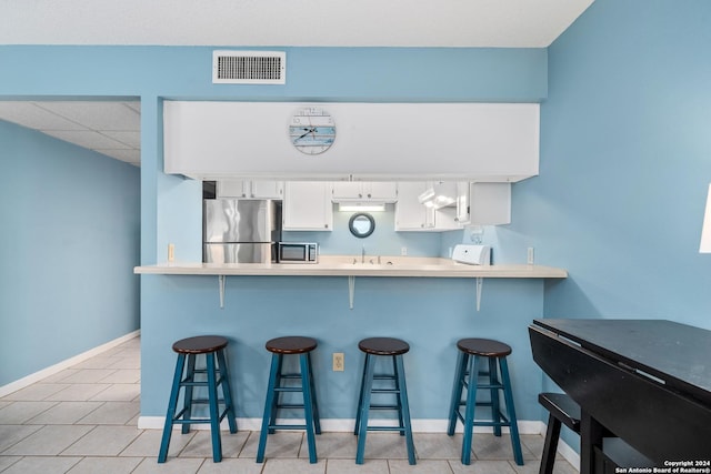 kitchen featuring white cabinetry, sink, a kitchen breakfast bar, kitchen peninsula, and stainless steel refrigerator