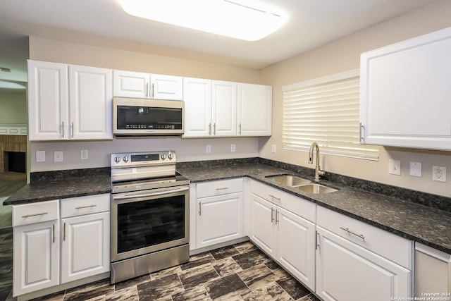 kitchen with appliances with stainless steel finishes, white cabinetry, dark stone countertops, and sink