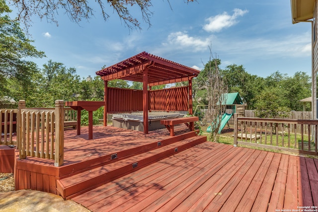 wooden deck with a jacuzzi, a pergola, and a playground