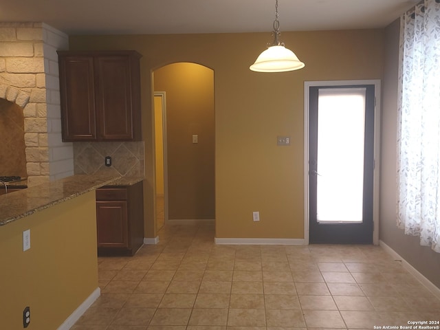 kitchen featuring backsplash, hanging light fixtures, light stone counters, and light tile patterned floors