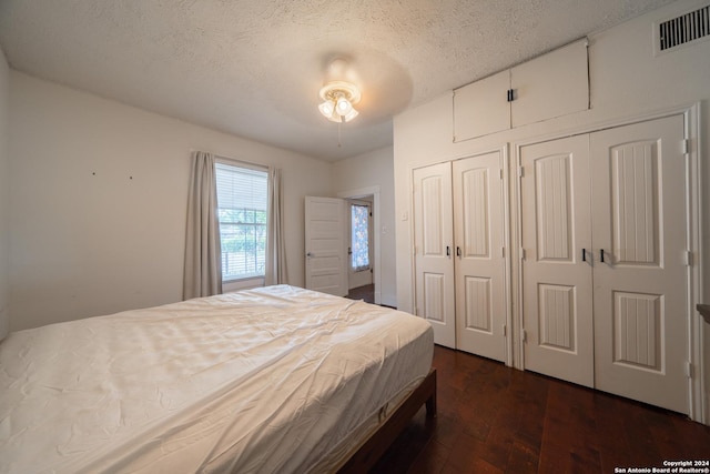 bedroom featuring ceiling fan, multiple closets, dark hardwood / wood-style floors, and a textured ceiling