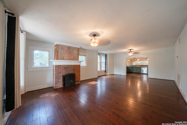 unfurnished living room with a brick fireplace, dark hardwood / wood-style flooring, and ceiling fan